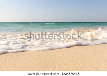 Waves on white sand beach. Sea shore on a sunny day in Arabian Gulf in Dubai. Relaxing happy background.