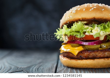 Close-up of delicious burger with lettuce, cheese, onion and tomato on dark background
