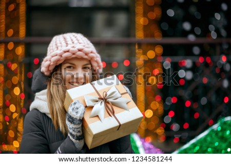 Romantic young woman wearing knitted pink cap and scarf holding gift box. Empty space