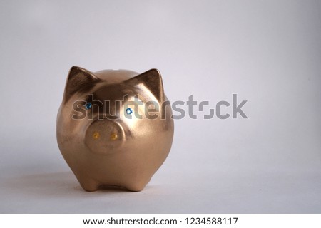 Gold ceramic piggy bank on the white background. Figurine of a gold piglet with blue shiny eyes. Place for inscription / text.