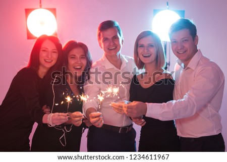 New year party, celebration and holidays concept - Young cheerful men and women holding burning sparklers
