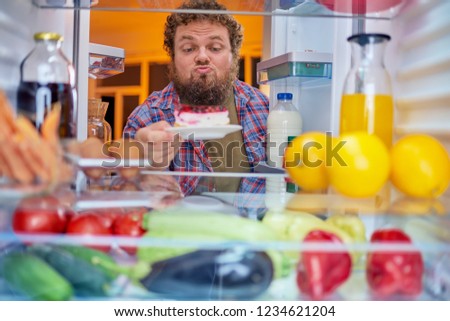 Man standing and taking gateau from fridge.  Picture taken from the inside of fridge.