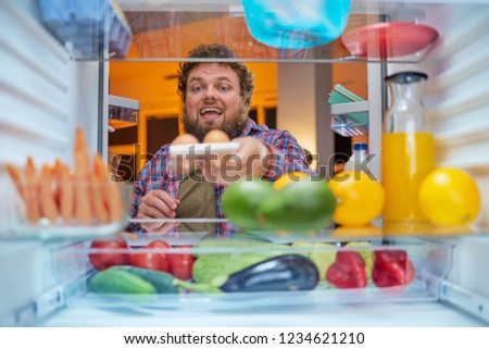 Man taking eggs from fridge to make a meal late at night. Unhealthy eating and eating disorder concept. Picture taken from the inside of fridge.