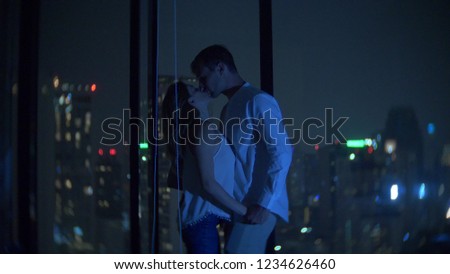 A young couple is kissing on the background of a panoramic window overlooking the city. Evening night time. background blur