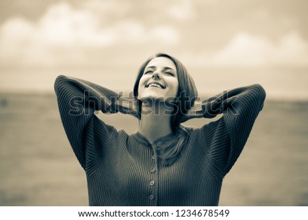 Beautiful adult girl in sweater at wheat field and cloudscape on background. Image in sepia color style