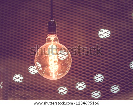 Tungsten orange light bulb hanging on the inside of the building with a black iron fence around,Lighting in buildings with multi-colored electric lamps,soft focus.Vintage colors picture,soft focus.