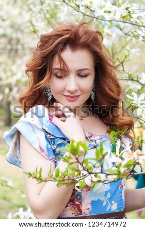 Beautiful woman with long dark wavy curls in a beautiful blue dress walk in the park among the lilacs and magnolias, spring concept, portrait, springtime