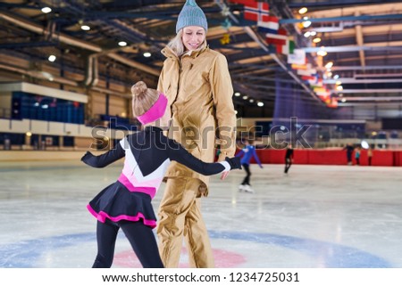 Back view portrait of little girl figure skating with smiling young mother in indoor rink, copy space