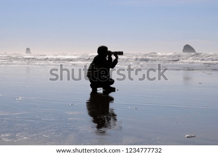 A silhouette of a man taking pictures of the ocean and horizon with a telephoto lens on  a beach. 