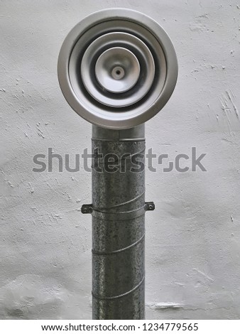Close-up of silver metal pipe with rounded output outside of building against white wall. 