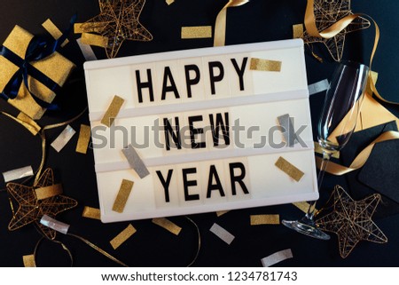 Happy New Year slogan on a lightbox with golden confetti decoration on black background. New Years Eve party. Flat lay. Top view. 2019