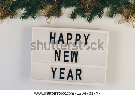 Happy New Year text displayed on a lightbox on the table with fir branches on the top. New Year concept.