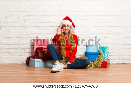 Girl with christmas hat and many gifts celebrating the christmas holidays showing an ok sign with fingers
