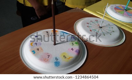 Solar or Sundial Clock is made up of several white sheets of paper on a table of brown and yellow.selective focus