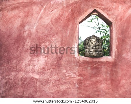 Small sitting Ganesha stone sculpture decoration on the space on grunge red cement wall with copy space.