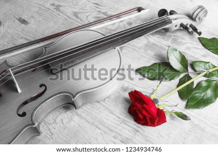 Violin, bow and red rose on a wooden textured table.