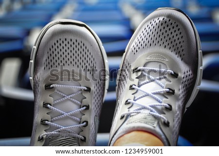 Close up top view of pair of ladies classic white sneakers with grey trim. Modern lifestyle footwear for men and women, with sporting venue in background.