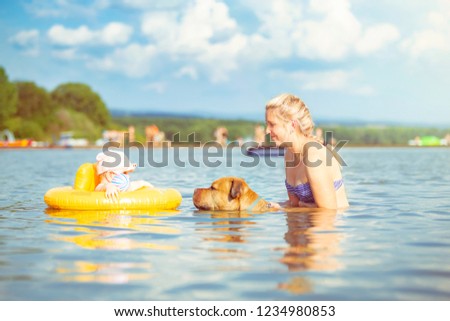 Mother, dog, and baby in the yellow inflatable ring are playing in a natural swimming pool. Vintage colors