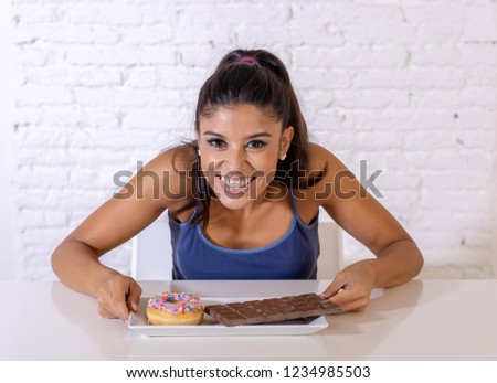 Young attractive latin woman sitting at table about to eat chocolate and doughnuts looking excited and happy in no more diet, sugar and chunky unhealthy food concept.