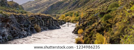 Water flowing through a canyon with steep rocky sides covered in autumn foliage