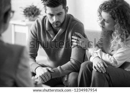 Black and white photo of supportive wife touching husband's arm during psychotherapy session for married people with problems