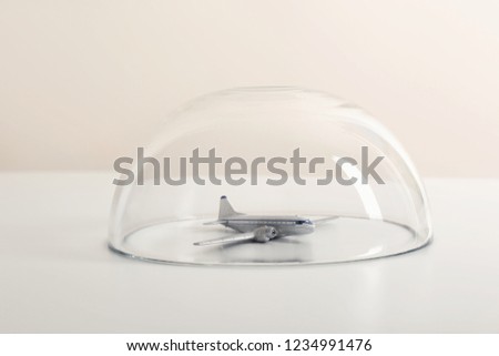 Toy plane under glass dome on white table. Travel insurance concept