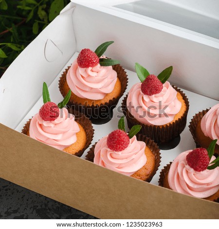 Cupcakes with raspberry cream, decorated with raspberries on top on gift wrap.