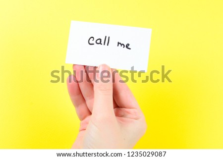 Call me text on a card in woman hand  on a yellow background.