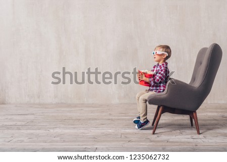 Little child in 3d glasses with popcorn in a chair