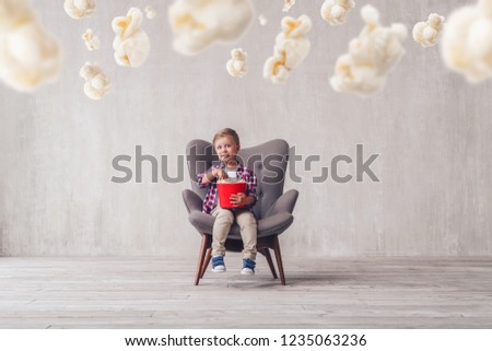 Smiling child eating popcorn in a cinema chair