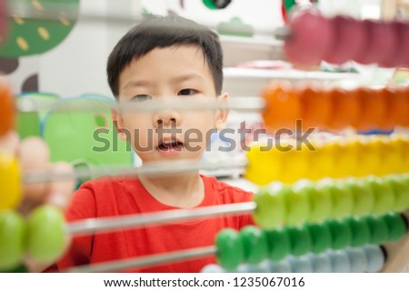 Close up shot of an Asian kindergarten boy having fun playing, moving colorful wooden abacus - purple, orange, yellow, green - learn through play, educational toy, child development concept