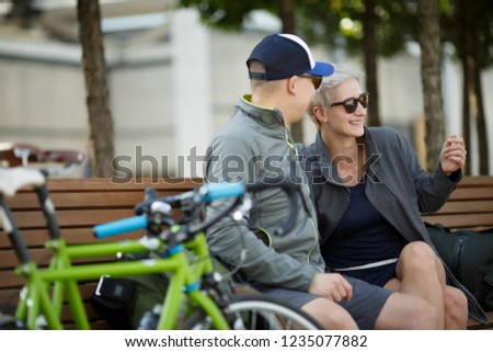 Picture of young man in sunglasses and blonde women sitting on bench next to bicycle