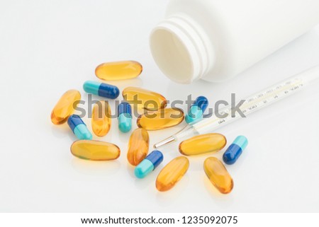 Medical : Close up of Yellow and Blue Capsules with Bottle and Analog Thermometer on White Background Shot in Studio.