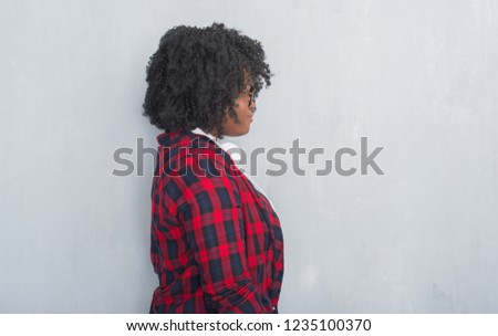 Young african american woman over grey grunge wall wearing headphones looking to side, relax profile pose with natural face with confident smile.