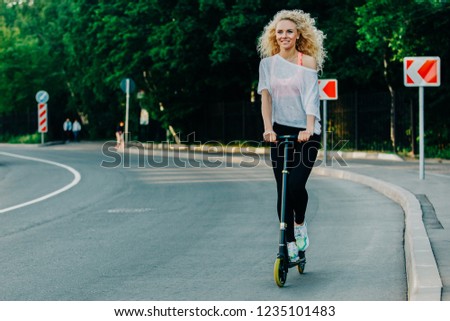 Full-length photo of curly-haired athletic woman kicking on scoo