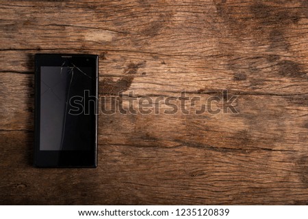 Smartphone with broken display screen is lying on the wooden table.