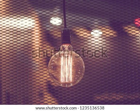 Tungsten orange light bulb hanging on the inside of the building with a black iron fence around,Lighting in buildings with multi-colored electric lamps,soft focus.Vintage colors picture,soft focus.