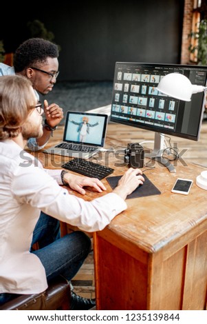 Two male photographers choosing woman's portraits at the working place with two computers in the studio