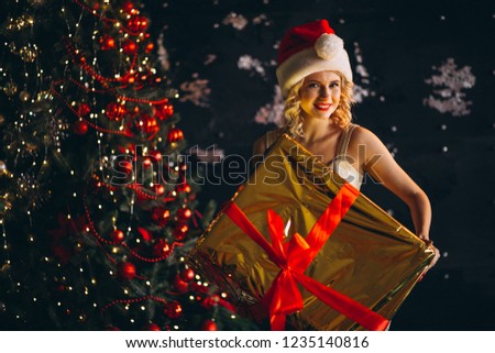Young woman in dress with Christmas presents by Christmas tree