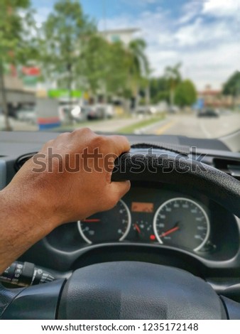 Hand of car driver holding steering wheel with dashboard panel speedometer and rpm gauge background and road traffic