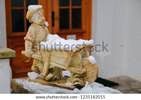 The photo was taken in Germany, on the street of the city of Garmisch-Partenkirchen. The picture shows a funny statuette of a boy with a wheelbarrow, covered with snow.
