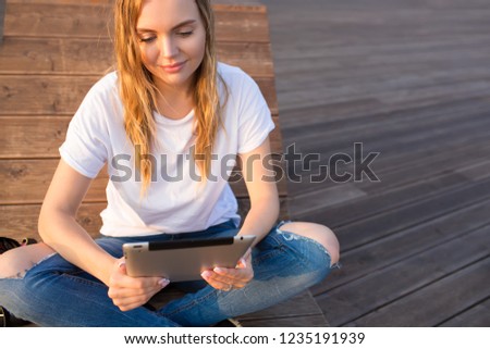 Pretty woman online shopping store via touch pad while sitting outdoors on wooden bench near copy space for advertising. Lovely female lifestyle blogger reading article via digital tablet 
