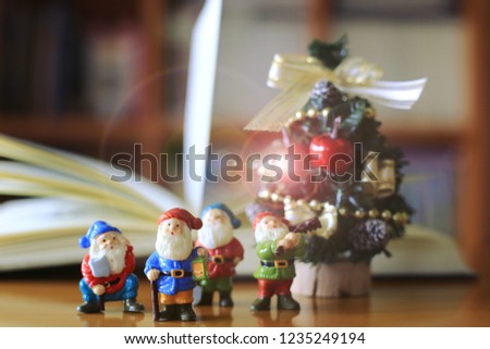 Santa doll on the table in the library. A small Christmas tree and open book is the background selective focus and shallow depth of field