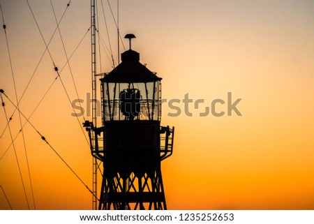 Abstract photo with industrial character of a lighthouse against a brightly colored sky with beautiful intense colors of the sunset. Minimalistic image with contrasts and the contours in the port