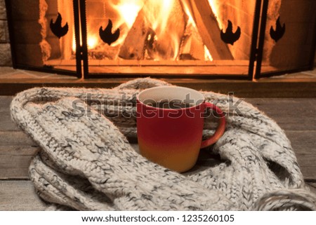 Cozy scene near fireplace with a Red cup with hot tea and cozy warm scarf.
