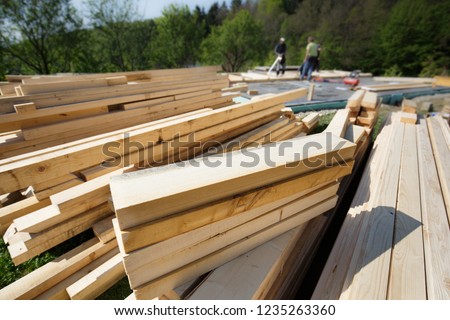 Pile of numbered, cut and prepared wood planks, beams and pieces for frame construction. Building process, construction site, carpentry, dry building industry concept with workers in the background. 