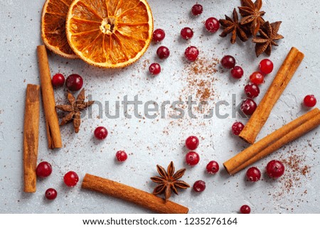 Close up view of winter flavour ingredients - cinnamon sticks, cranberries, anise stars, dried oranges, all laid out on a flat table topped with sugar and chocolate powder.
