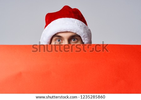 Poster mockup  a man in a holiday hat is standing behind an orange sheet of paper                        