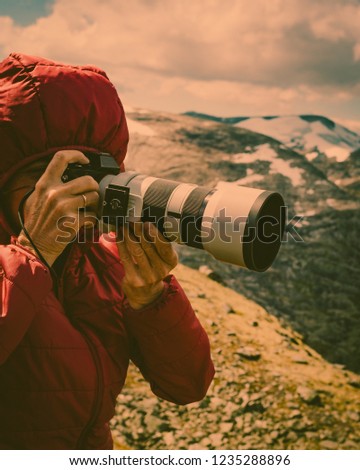 Female tourist taking photo with camera, enjoying mountains landscape from Dalsnibba area in Norway.