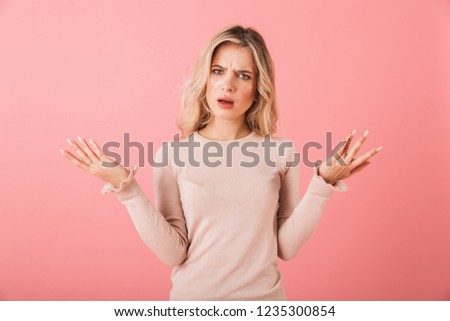 Portrait of an upset young woman wearing sweater standing isolated over pink background, shrugging shoulders